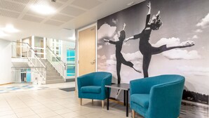 Un vestíbulo con sillones azul turquesa, una escalera y un mural de bailarines.
