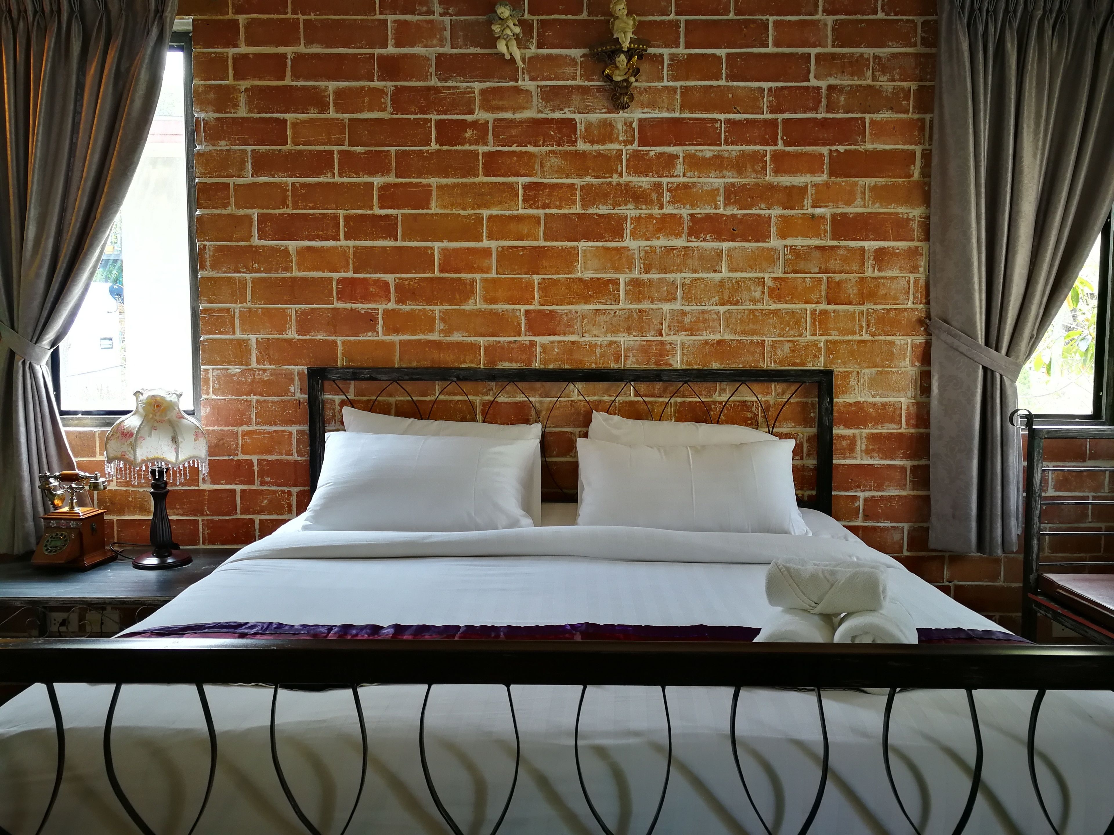 A bed with white linens, a brick wall, and a window with curtains.
