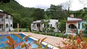 A pool area with a view of two-story buildings, surrounded by greenery and hills. - Stamp Hills Resort & Restaurant (Suan Phueng)