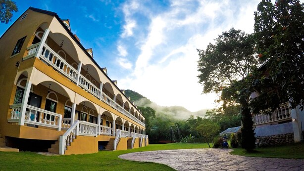 A building with multiple balconies, a stone pathway, and lush greenery. - Stamp Hills Resort & Restaurant (Suan Phueng)
