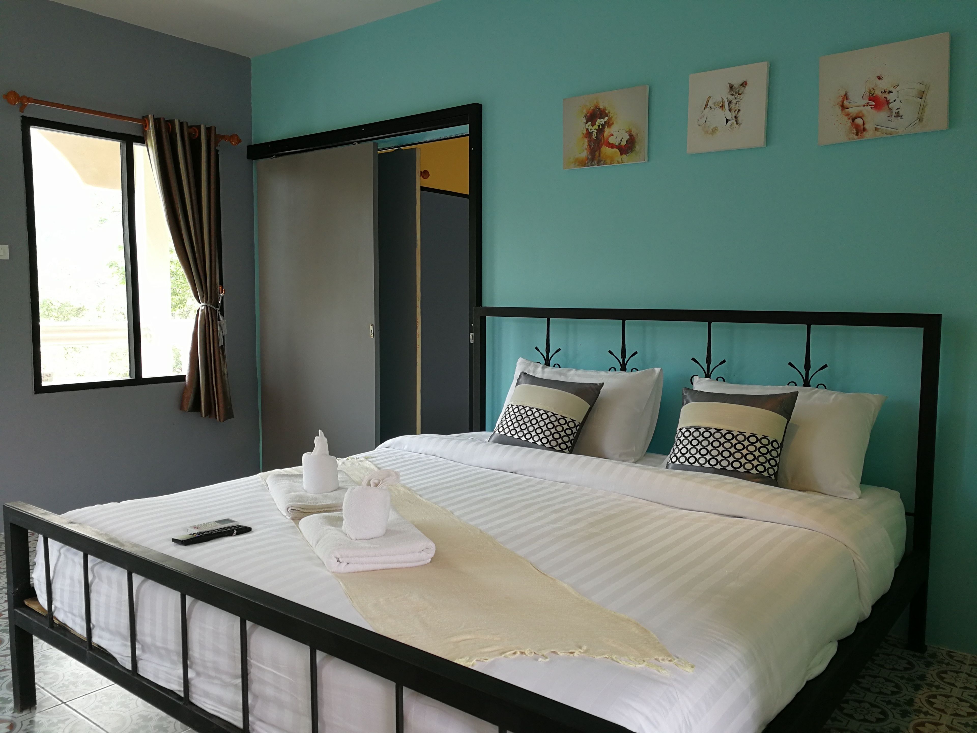 A neatly made bed with pillows, a remote control, and towels on a bed with a black frame.