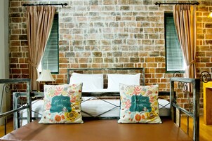 A bed with two decorative pillows, a brick wall, and a window with curtains.