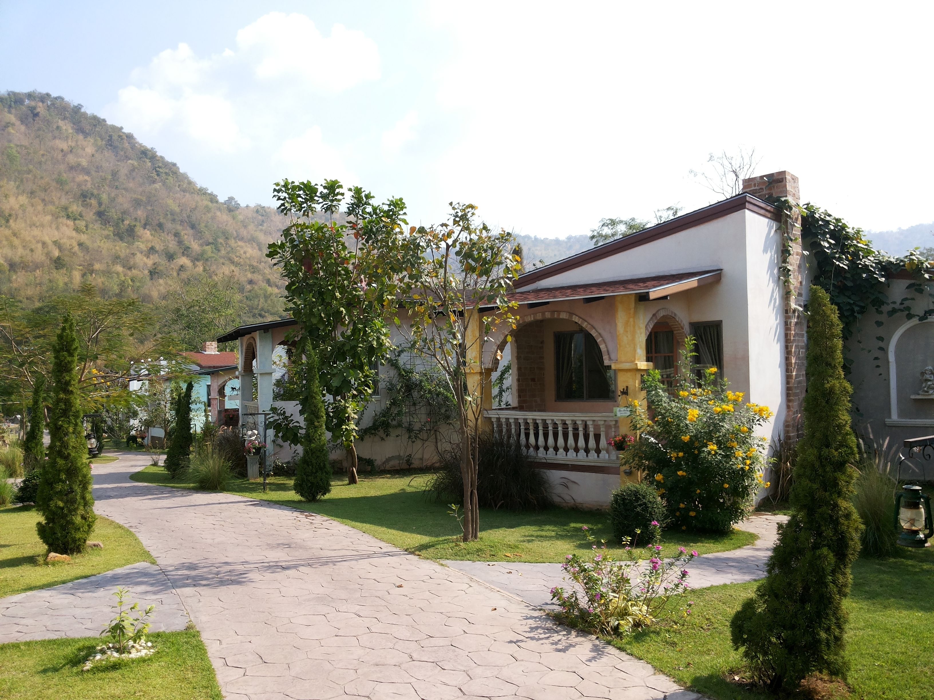 A building with a paved pathway leading to it, surrounded by greenery and a mountainous backdrop.