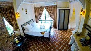 A hotel room with a bed, a small table with a lamp, a wardrobe, and a kitchenette. - Stamp Hills Resort & Restaurant (Suan Phueng)