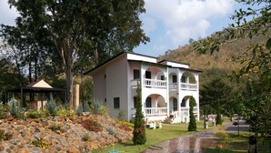 A two-story building with a white exterior, multiple balconies, and a stone pathway leading to the entrance. - Stamp Hills Resort & Restaurant (Suan Phueng)