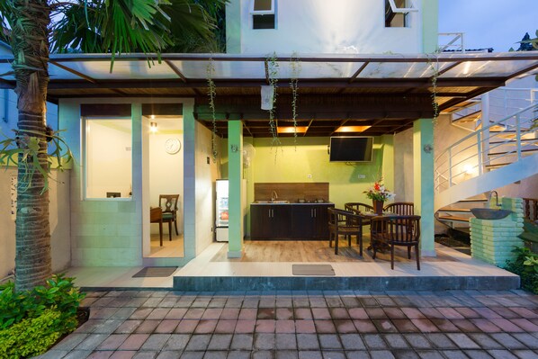 A modern house with a covered outdoor kitchen area, a dining set, and a staircase.