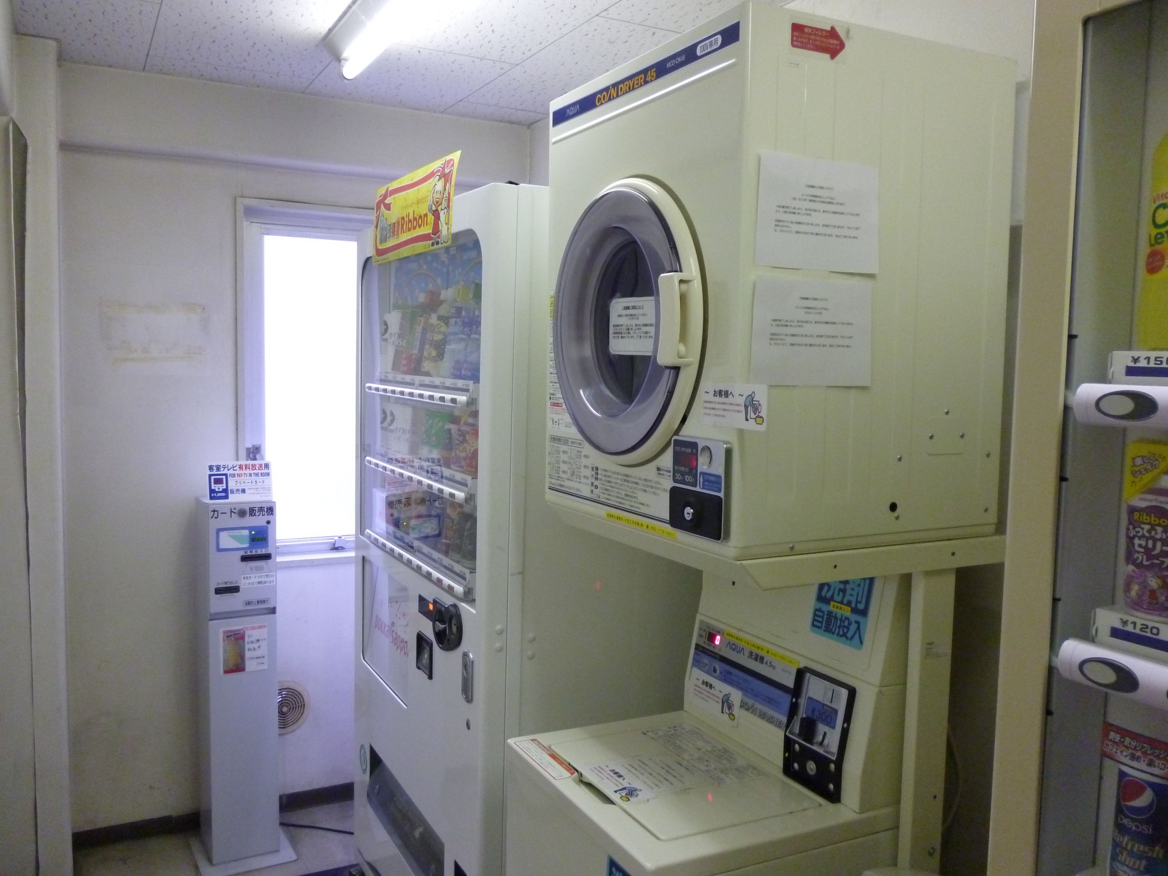 A laundromat with stacked washers and dryers, a vending machine, and a door leading to another room.