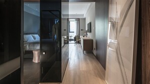 A modern hotel room with a bed, a desk, and a chair. There is a window with curtains and a view of the outside.