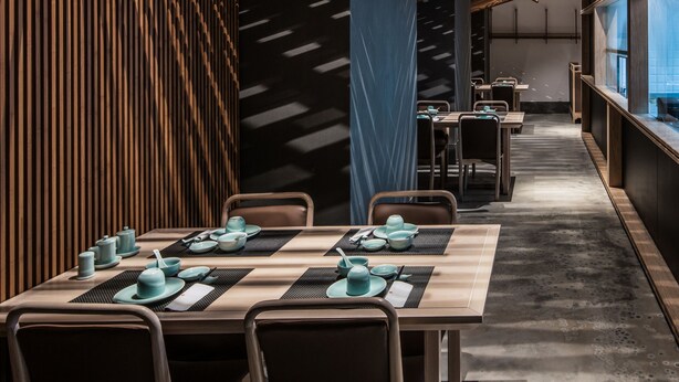 A modern restaurant interior with wooden slatted ceilings, long tables, and chairs.