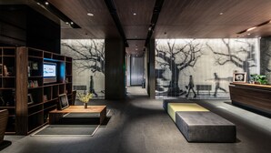 A modern lobby with a wooden reception desk, a seating area with a bench, and a bookshelf with books and a small plant.