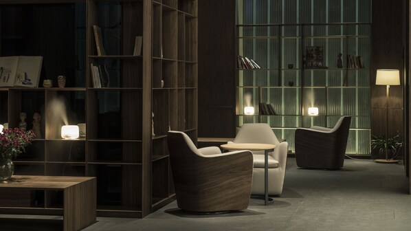 A modern lounge area with a wooden bookshelf, two armchairs, a small round table, and a floor lamp. - The Nook Hotel Hangzhou (Hangzhou)