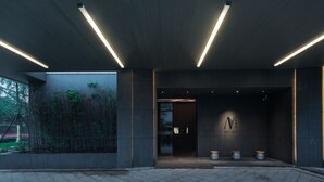 A modern building entrance with a dark facade, a glass door, and a logo on the wall.