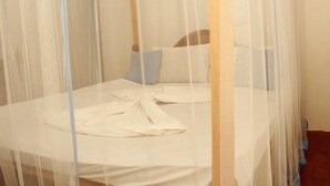 Una cama individual con sábana blanca y dos almohadas, cubierta por un dosel blanco transparente.