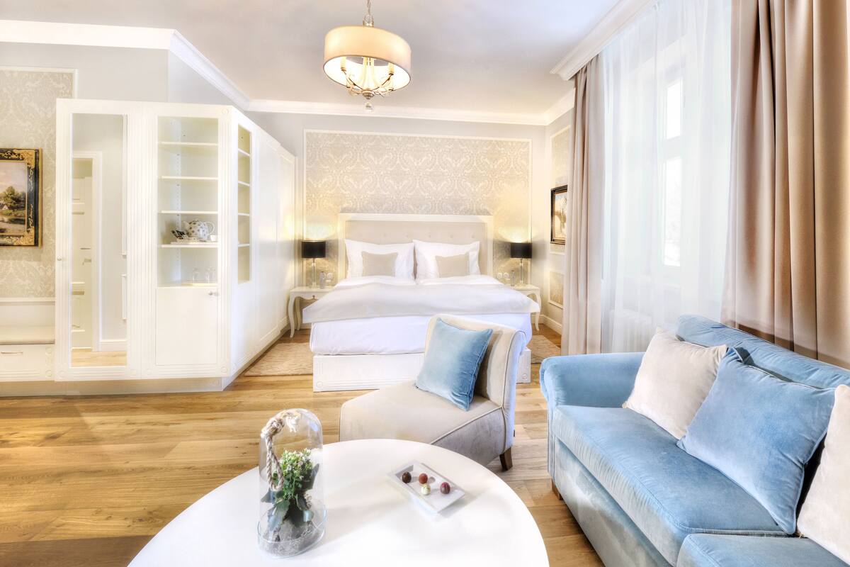 Een hotelkamer met een groot bed, een zithoek met een blauwe bank, een witte salontafel en een kroonluchter.