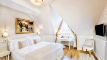 Un dormitorio con una cama grande, una mesita de noche, un escritorio pequeño con una silla, un ventanal y un televisor instalado en la pared.