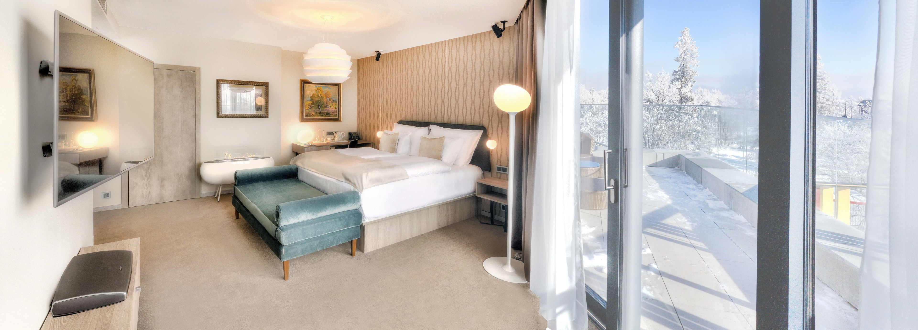 Une chambre d’hôtel moderne équipée d’un lit, d’une banquette, d’une table de chevet et d’une grande fenêtre donnant sur la ville.