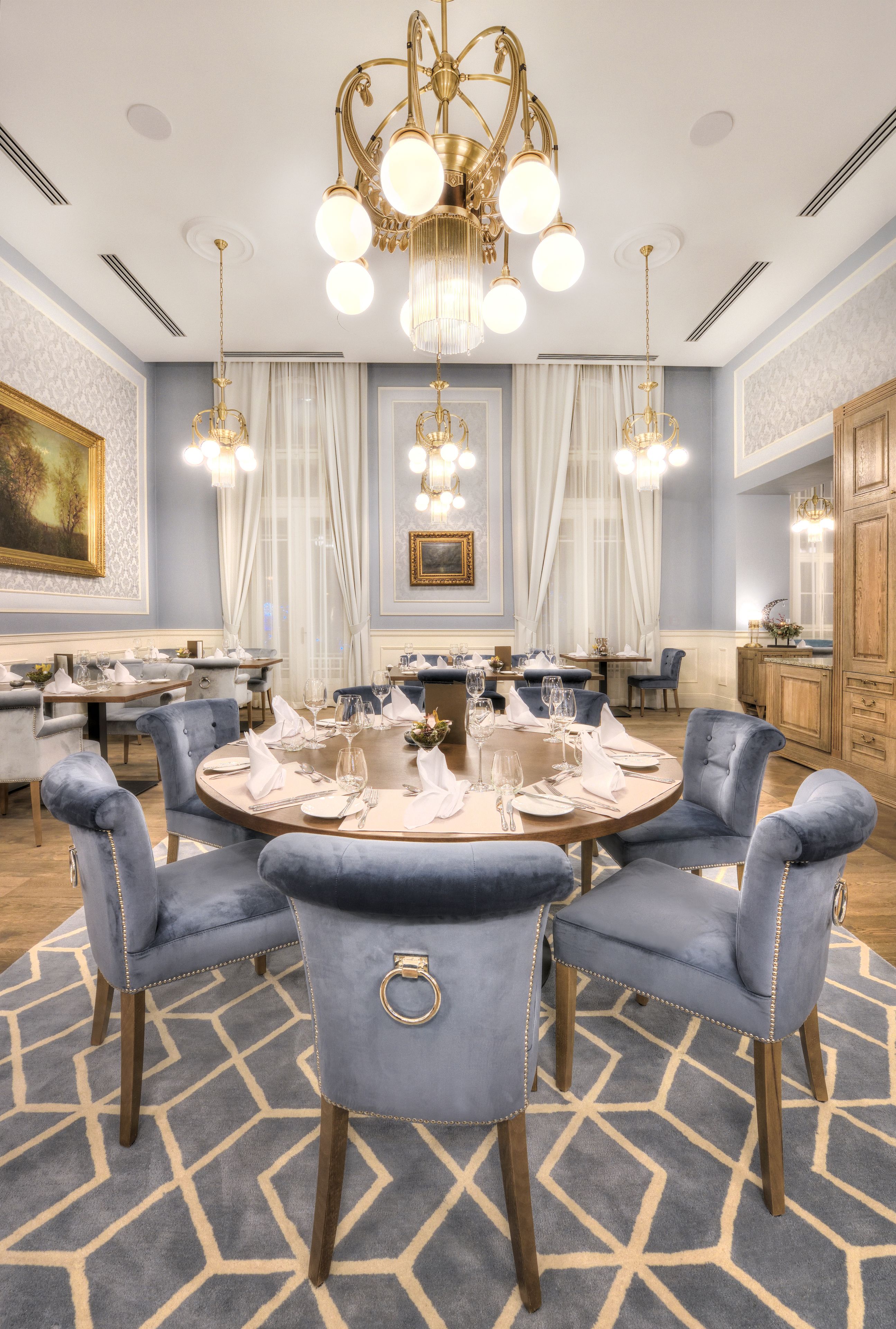 Une salle à manger élégante, avec une table ronde, des chaises recouvertes d’un tissu bleu et un lustre.