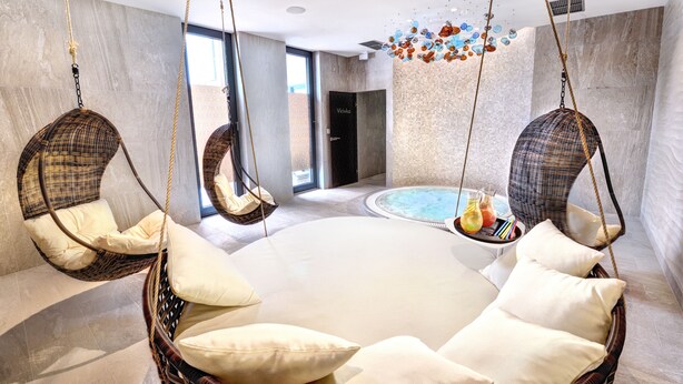 A circular hot tub with wicker chairs and cushions around it, a tiled floor, and a modern interior design.