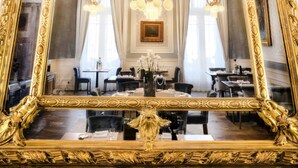 A grand room with a large ornate mirror, elegant chandelier, and a dining area with tables and chairs.