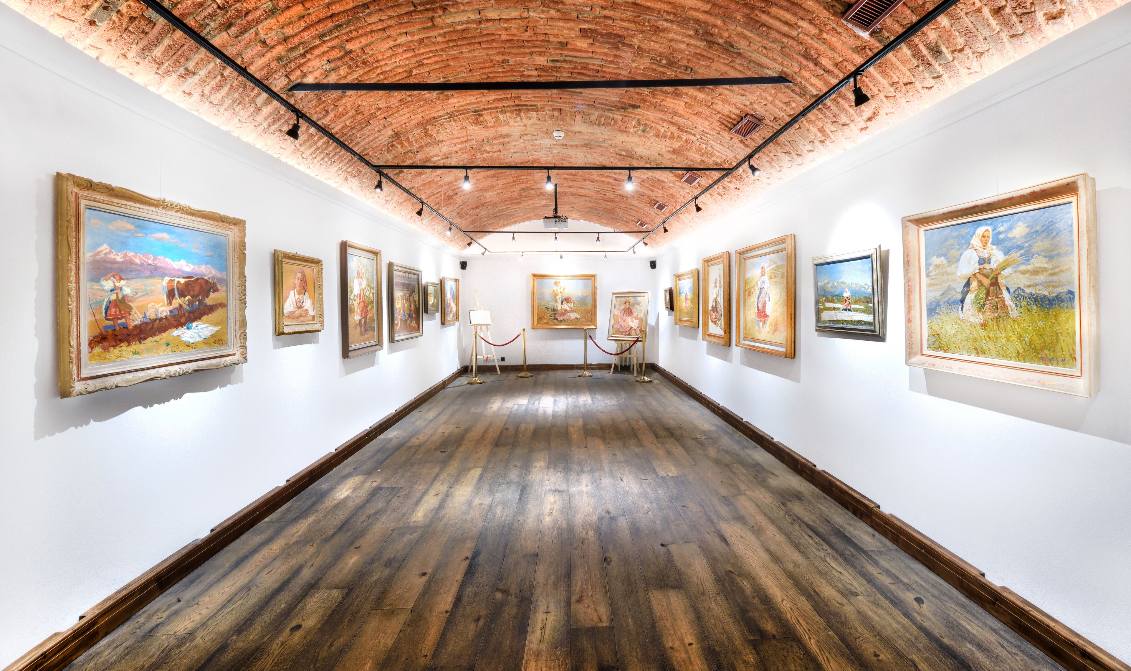 A gallery with paintings on the walls and a wooden floor.