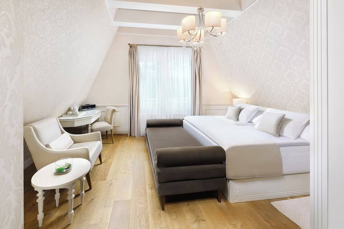 Een compacte hotelkamer met een bed, een klein bureau, een stoel en een bankje.
