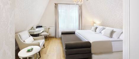 A compact hotel room with a bed, a small desk, a chair, and a bench.