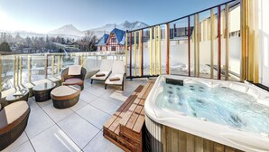 A rooftop terrace with wicker furniture, a hot tub, and a view of snow-capped mountains.
