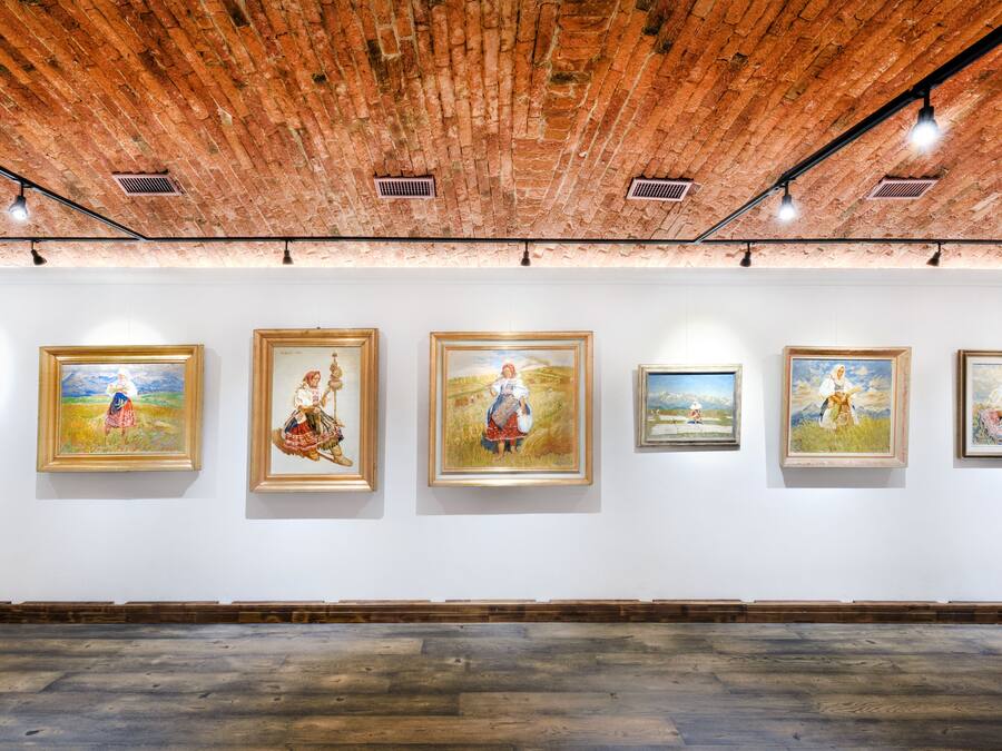 Een galerij met zes ingelijste schilderijen aan witte muren en een houten vloer.