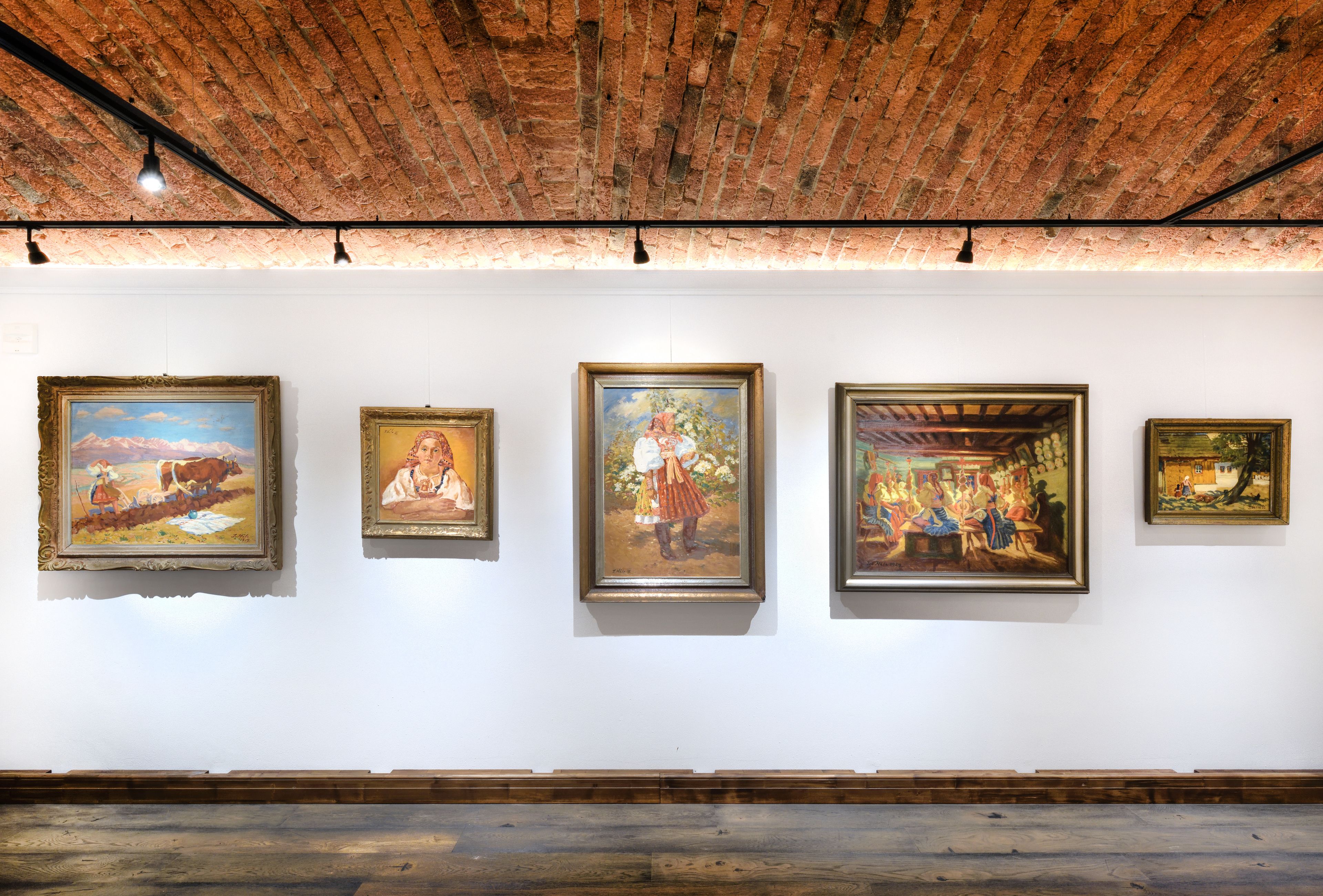 Une galerie où sont exposées quatre peintures encadrées sur un mur blanc.