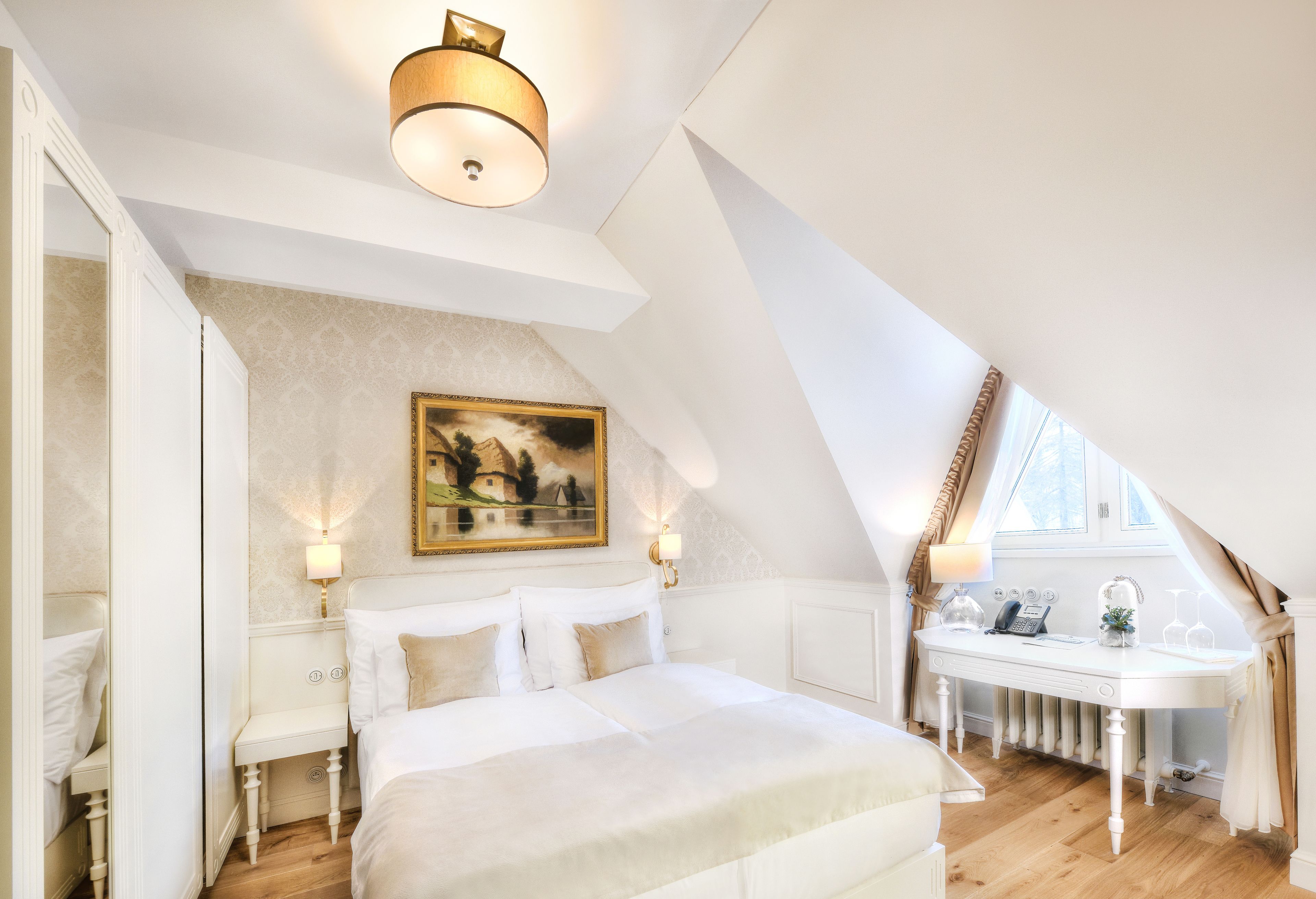 Une chambre à coucher avec un grand lit, des tables de chevet, un bureau avec une chaise, un tableau au mur et une fenêtre avec des rideaux.