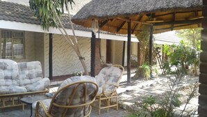 A covered outdoor seating area with wicker chairs and a sofa, a thatched roof, and a tiled floor. - Road View Lodge (Francistown)
