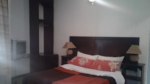 A hotel room with a bed, two bedside tables, a nightstand, a lamp, and a wall-mounted light fixture. - Road View Lodge (Francistown)