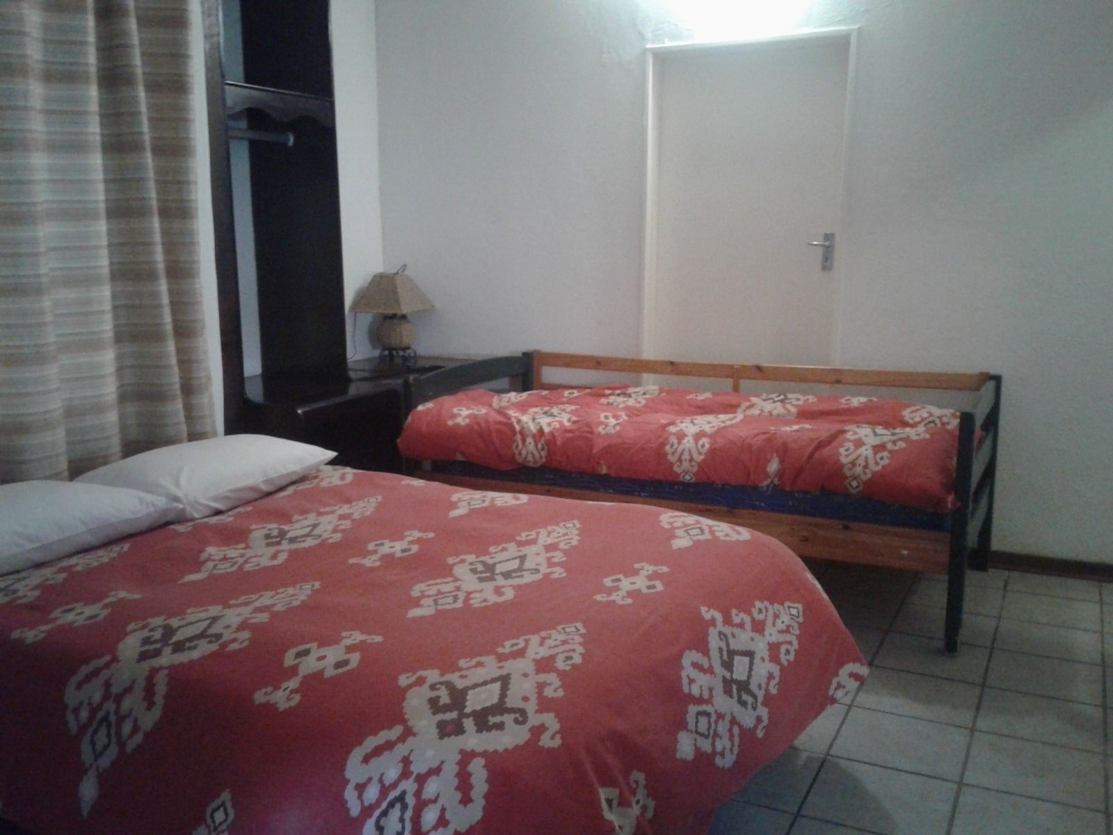Une chambre avec deux lits simples, une table de chevet, une lampe et une porte.