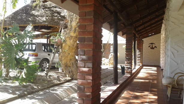 A covered outdoor area with brick pillars, a tiled floor, and a thatched roof structure. - Road View Lodge (Francistown)