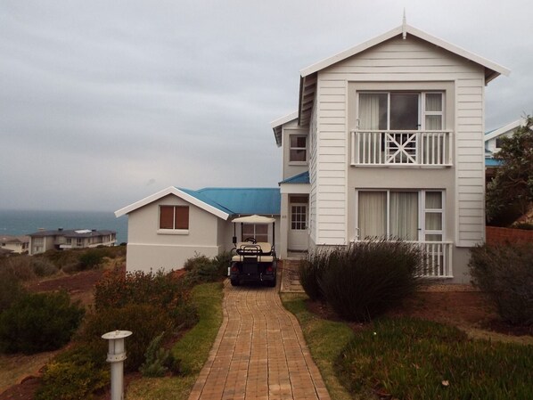 A two-story white building with a balcony, a golf cart in front, and a view of the ocean.