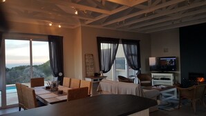 A spacious living room with a large window, a fireplace, and a television. - Pinnacle Point Pool Lodge (Mossel Bay)