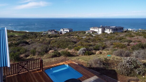 A pool on a wooden deck with a view of the ocean and houses in the background. - Pinnacle Point Pool Lodge (Mossel Bay)