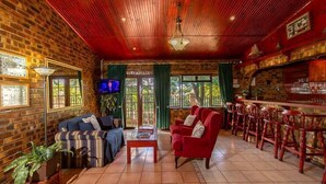 A cozy room with brick walls, a red ceiling, a television, a sofa, a red armchair, and a bar area with stools. - La Mer Lodge (Richards Bay)