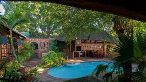 A pool area with a brick structure, seating, and lush greenery. - La Mer Lodge (Richards Bay)