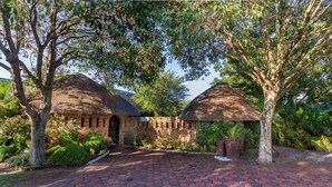 A traditional thatched-roof house with a paved pathway leading to it, surrounded by lush greenery. - La Mer Lodge (Richards Bay)