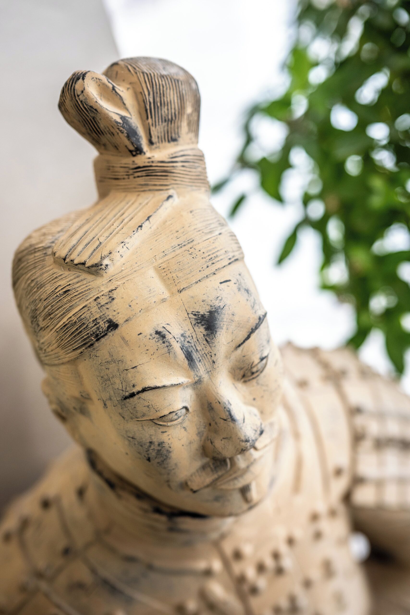 A close-up of a weathered, beige-colored sculpture with intricate carvings, possibly depicting a historical figure or deity.