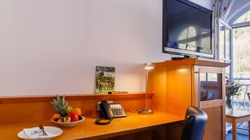 Habitación de hotel con un escritorio de madera, un teléfono, un frutero, un cuadro enmarcado y un televisor.