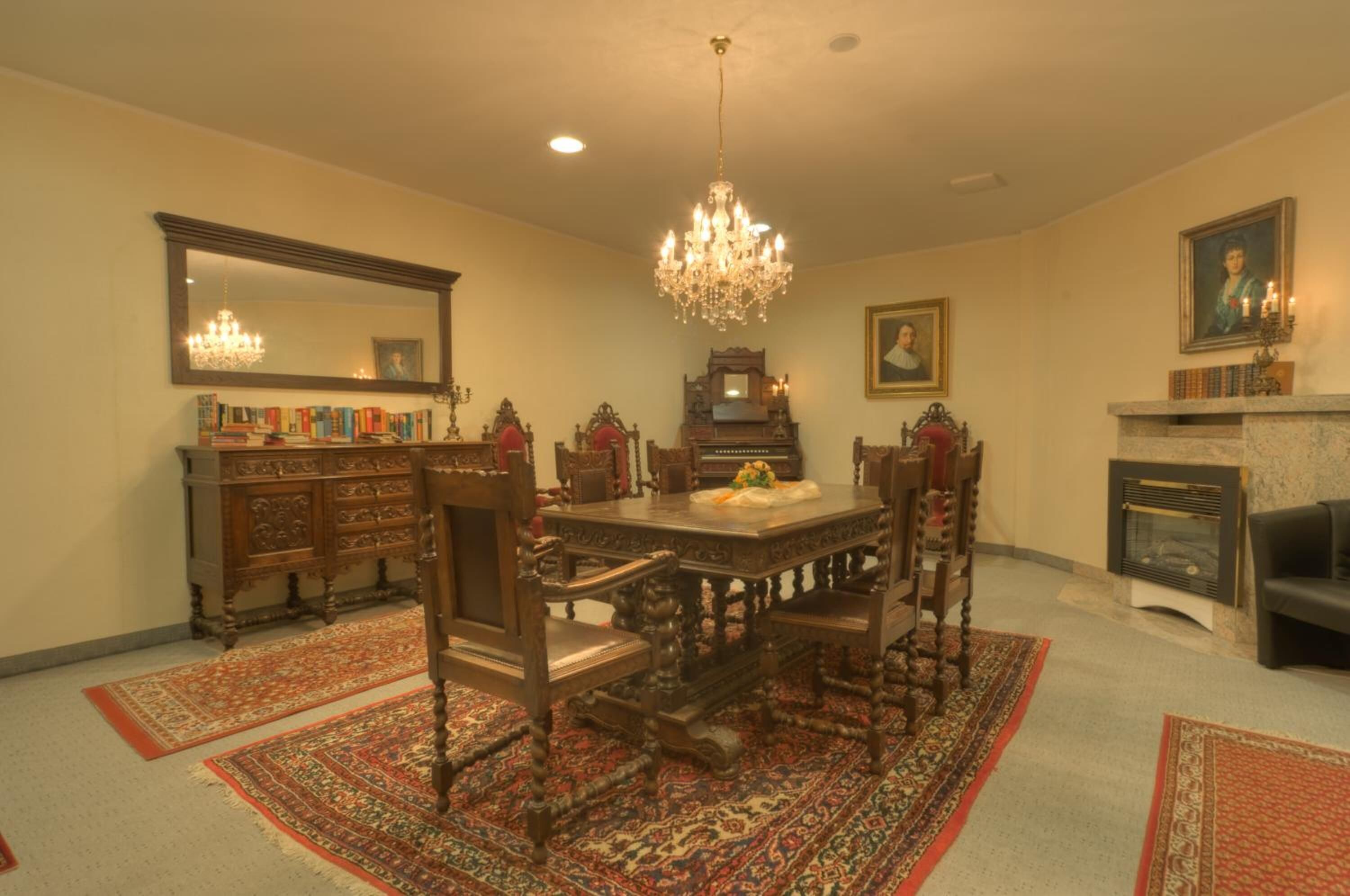 A formal dining room with a wooden table, chairs, a chandelier, a fireplace, and a large mirror.