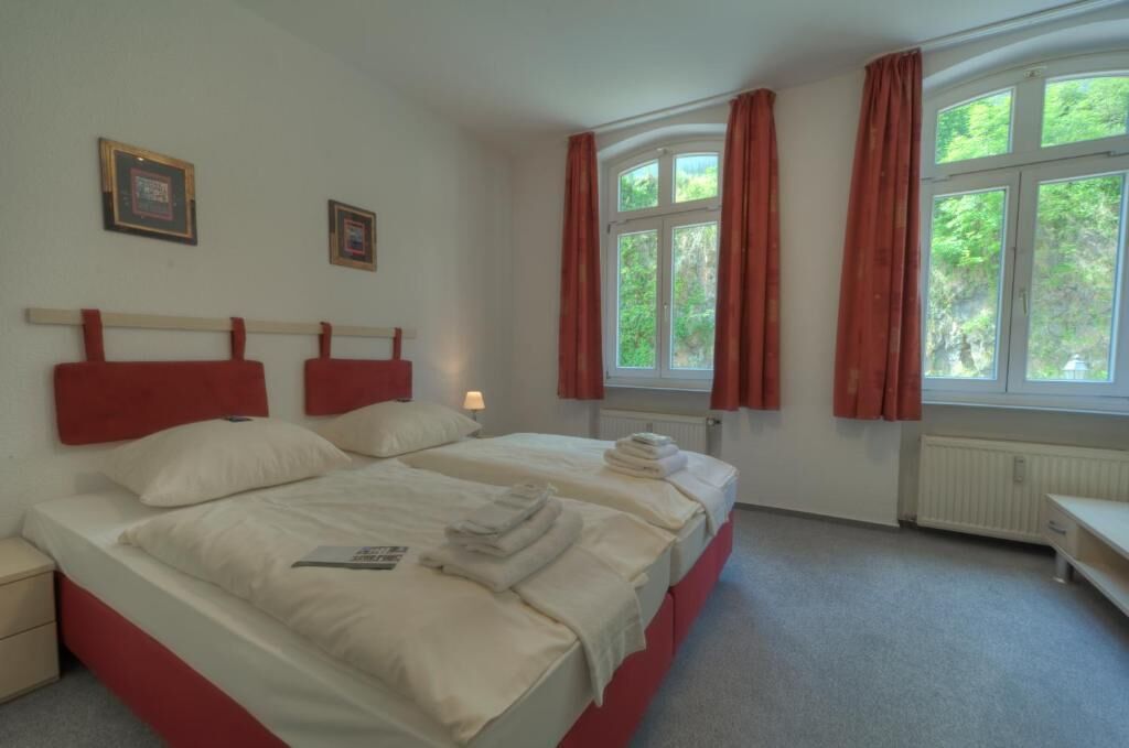 A hotel room with two beds, red headboards, white bedding, a nightstand, a window with curtains, and framed pictures on the wall.
