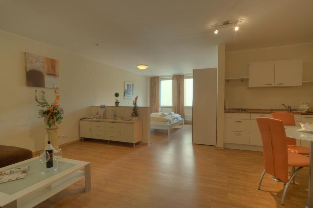 Eine moderne Wohnung mit Wohnzimmer, Essbereich und Küche. Es gibt ein Sofa, einen Esstisch mit Stühlen und eine Küchenzeile.