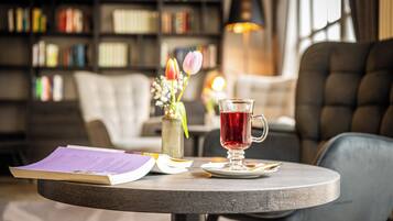 A round wooden table with a book, a glass of red beverage, and a vase with flowers.