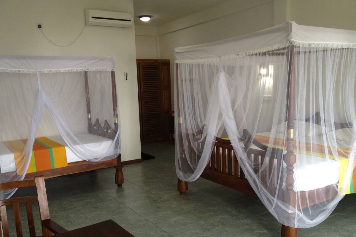 Two single beds with mosquito netting, wooden headboards, and a tiled floor.