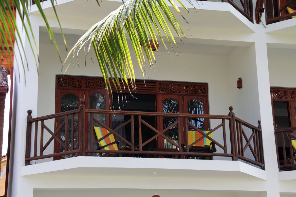 A multi-story building with balconies, wooden railings, and a palm tree.