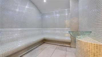 Un baño con paredes de azulejos, un banco de vidrio y un lavabo de vidrio.