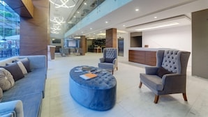 Un vestíbulo espacioso con un diseño moderno, que incluye una zona de estar con sofás y sillones, un otoman redondos y un mostrador de recepción.